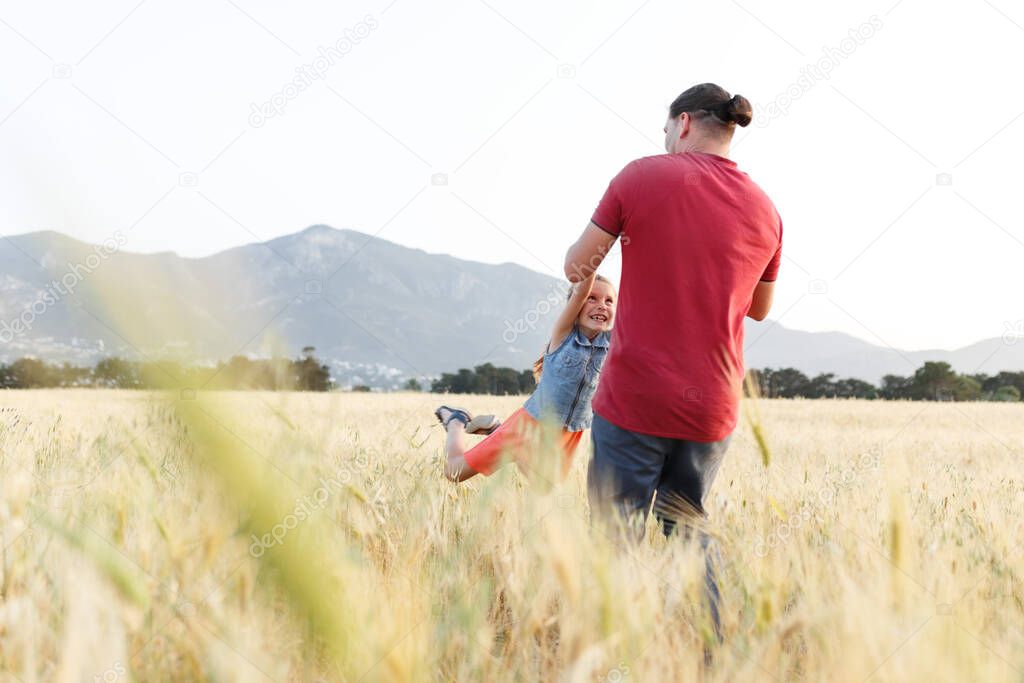 Dad spins his daughter on field , having fun at sunset. Father plays with child. Happy family and childhood concept. 