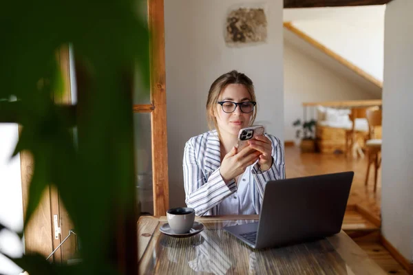 Happy young businesswoman sitting at table with laptop, holding mobile phone call with client in office. Skilled manager saleswoman calling customer, giving professional consultation.