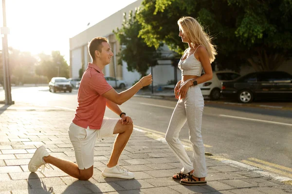 Young man with engagement ring making proposal to his beloved girlfriend outdoors.