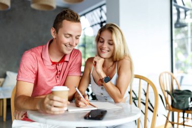 Üniversitenin kafe masasında oturup ödev yapan ya da plan yazan mutlu öğrenciler. Genç kadın ve erkek kahve fren sırasında birlikte vakit geçirip notlar alıyorlar..