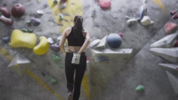 Chica deportiva escalador de roca se dedica a la escalada en roca en el gimnasio. Utiliza magnesio en una bolsa de tela. Escala una pared con obstáculos, trenes. — Vídeo de stock