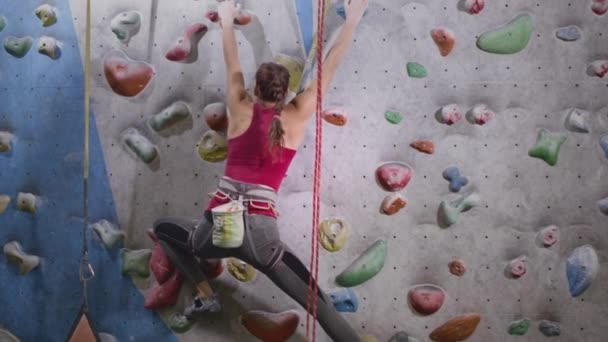 Esporte atlético mulher escalada parede de escalada, praticando sozinho no ginásio indoor. Uma garota experiente está usando um cabo de segurança e magnésio — Vídeo de Stock