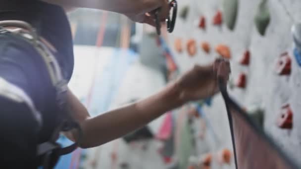 Sport atletische vrouw beveiligt het veiligheidstouw, karabijnhaak. Bevestigt de belay aan de karabijnhaak. Solo klimmen in een indoor gym. Langzame beweging — Stockvideo