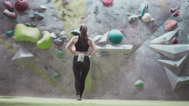 Sportowa dziewczyna wspinaczka jest zaangażowana w wspinaczkę na siłowni. Używa magnezu w torbie. Wspina się na ścianę z przeszkodami, pociągi. — Wideo stockowe