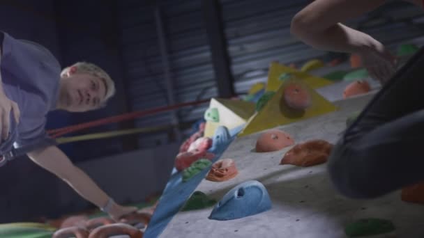 Sport girl and athletic man climbers give five on the climbing wall in the gym. Uses a safety rope and clothing on the bouldering wall — Stock Video
