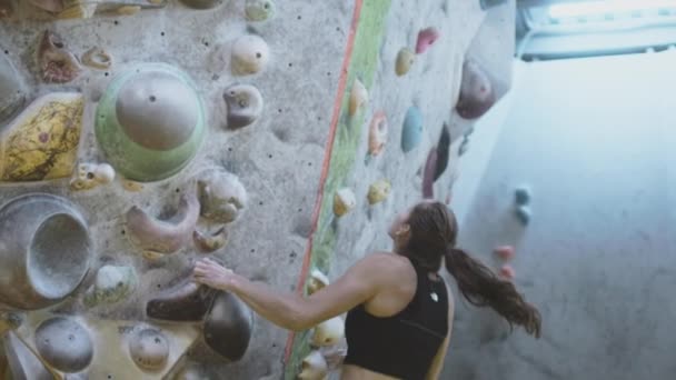 Deporte atlético chica salto sube por la pared de escalada en el gimnasio. Utiliza una cuerda de seguridad en la pared de cantos rodados, y usa un zapato de escalada — Vídeos de Stock