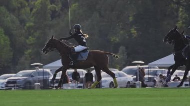 UFA RUSSIA - 05.09.2021: At üstündeki polo oyuncusu, yavaş çekim. Uzun saplı tahta bir tokmak tutuyor. İzleyicilerle maç, yeşil çimen sahası