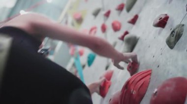 Sportif kız kaya tırmanışçısı spor salonunun yapay duvarına asılmış. Taşları ve çıkıntıları tutan atletik kadın. Şehirde kayalık bir yer. Yavaş çekim