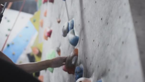 Sportig flicka bergsklättrare är engagerad på en konstgjord vägg i gymmet. Athletic Woman Fånga stenar och avsatser. Bouldering i staden. Långsamma rörelser — Stockvideo