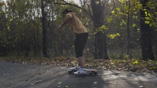 Egy fém bionikus műlábú fiatalember gördeszkázik az őszi erdőben. Egy műláb lelöki az aszfaltot egy gördeszkáról. — Stock videók
