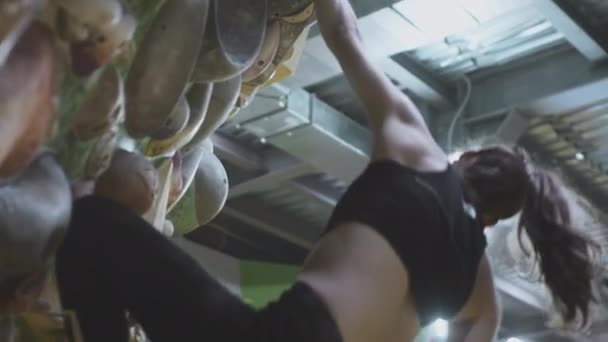 Sport atletyczna dziewczyna skacząc w górę wspina się na ścianę wspinaczkową w siłowni. Używa liny zabezpieczającej na ścianie głazu. Chwyta kamienie dłonią — Wideo stockowe