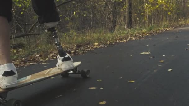 Een jongeman met een metalen kunstbeen rijdt op een skateboard in een herfstpark. Ga sporten met een kunstbeen — Stockvideo