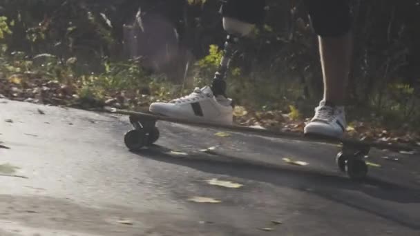 Un joven con una pierna protésica de metal monta un monopatín en un parque de otoño. Ir a los deportes con una pierna artificial — Vídeos de Stock