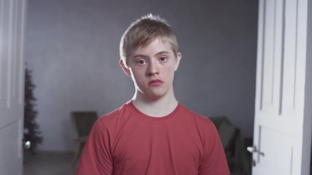 Portrait of a child boy with down syndrome. The teenager smiles, looks into the camera. Disabled person at home. Life with a disability — Stock Video