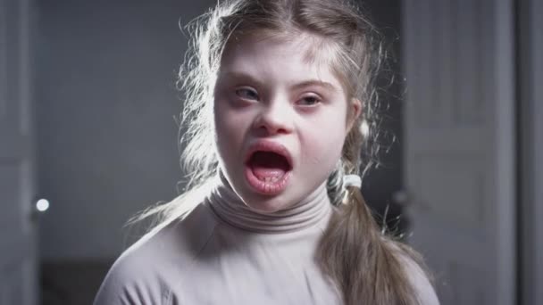 Портрет девочки с синдромом Дауна. Подросток улыбается, смотрит в камеру. Инвалид дома. Жизнь с инвалидностью — стоковое видео