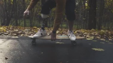 Metal protez bacaklı genç bir adam sonbahar parkında kaykaya biniyor. Yapay bacakla spor yapmaya git.