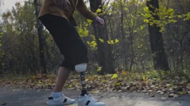 Metal protez bacaklı genç bir adam sonbahar parkında kaykaya biniyor. Yapay bacakla spor yapmaya git.