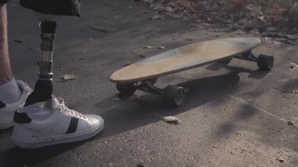 Un giovane uomo con una protesi metallica cavalca uno skateboard in un parco autunnale. Entra nello sport con una gamba artificiale — Video Stock