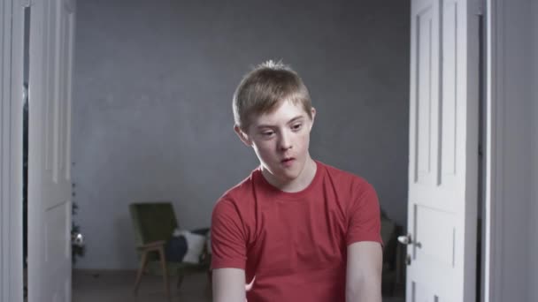 Portrait of a child boy with down syndrome. The teenager smiles, looks into the camera. Disabled person at home. Life with a disability — Stock Video