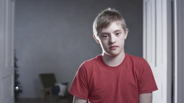 Portrait of a child boy with down syndrome. The teenager smiles, looks into the camera. Disabled person at home. Life with a disability — Stock Video