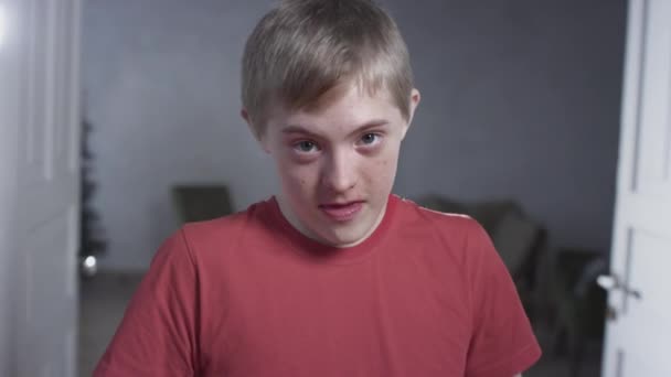 Portrait of a child boy with down syndrome. The teenager smiles, looks into the camera. Disabled person at home. Life with a disability — Stock Video