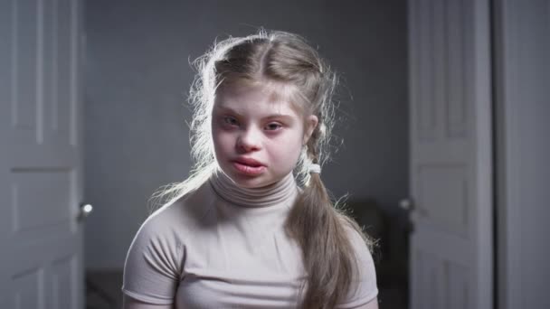 Portrait of a child girl with down syndrome. The teenager smiles, looks into the camera. Disabled person at home. Life with a disability — Stock Video