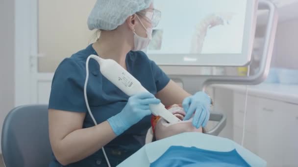 El doctor escanea los dientes de los pacientes en la clínica. El dentista sostiene en su mano un escáner 3D manual para la mandíbula y la boca. Salud dental. Crea un modelo 3D de dientes y encías en un monitor médico — Vídeo de stock