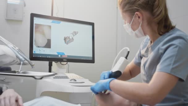 Doktor klinikteki hastaların dişlerini tarıyor. Diş hekimi elinde çene ve ağız için bir 3D tarayıcı tutuyor. Diş sağlığı. Tıbbi monitörde 3 boyutlu diş eti ve diş eti modeli oluşturur — Stok video