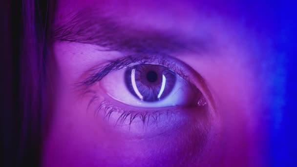 Extreme close-up Beautiful girl opens one eye, neon pink blue light. Attractive feminine look. Party nightclub, fashion show. Macro slow motion
