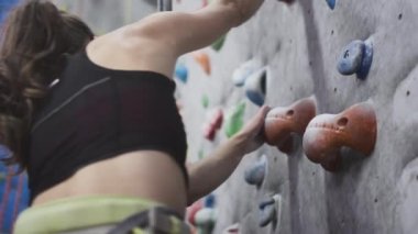 Sportif kız kaya tırmanışçısı tırmanma duvarına tırmanır. Güvenlik ipi ve tırmanma kıyafeti kullanıyor. Taşların ve çıkıntıların üzerinde el ele tutuşur