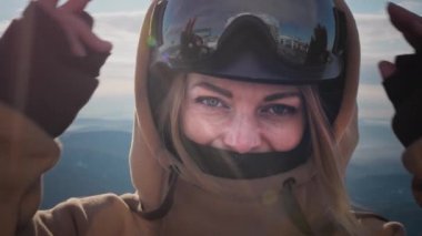 Güzel bir kız kış gözlüğü takar ya da snowboard yaparken maske takar. Büyük mavi gözler. Rüzgarda ağır çekimde hareket eden sarı saçlar. Tatil köyünde seyahat