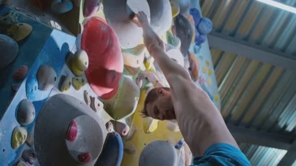 Athletic male rock climber climbs an artificial rock climbing wall. A strong experienced athlete practices bouldering wall climbing inside a gym — Stock Video