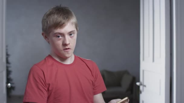 Retrato de un niño con síndrome de Down. El niño sostiene un teléfono inteligente con las manos, juega juegos móviles en la aplicación. Una persona con necesidades especiales — Vídeos de Stock