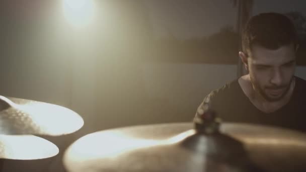 En ung attraktiv manlig trummis spelar med en pinne på ett trumset. Det slår mot cymbaler. Hemmastudio för inspelning av ljud och sånger. — Stockvideo