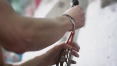 Sportif bir adam kemeri vücuduna bir karabinayla bağlar. Kayalık duvara tırmanmaya hazır. Beyaz adam emniyet kemerine karabina takıyor.