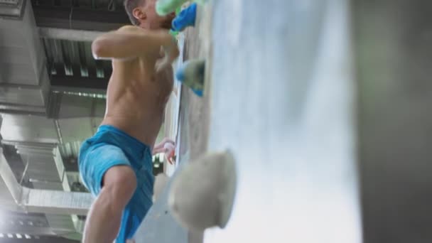 Homem atlético caucasiano sobe a parede de pedra. Práticas de escalada em uma parede interior artificial. Esportes radicais, estilo de vida ativo — Vídeo de Stock