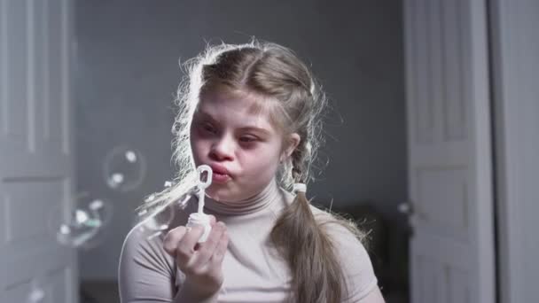 Portrét dívky s Downovým syndromem. Dítě drží mýdlové bubliny s rukama, nafoukne a raduje se. Chromozomální genetická porucha u dítěte. — Stock video