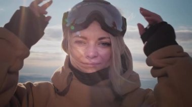 Güzel bir kız kış gözlüğü takar ya da snowboard yaparken maske takar. Büyük mavi gözler. Rüzgarda ağır çekimde hareket eden sarı saçlar. Tatil köyünde seyahat