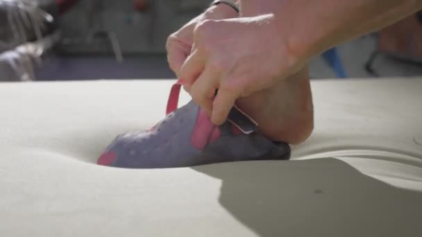 Hombre deportivo escalador de roca se pone zapatos de escalada, calzado diseñado para escalada en roca. Le pone botas en los pies. Preparación para escalar en el gimnasio — Vídeos de Stock