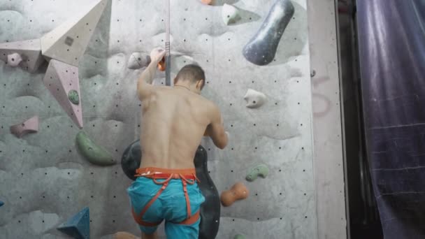 Athletic male climber quickly climbs an artificial climbing wall. Speed lift. A strong experienced rock climber practices boulder wall climbing inside — Stock Video