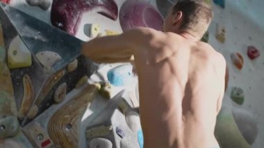 Güçlü bir atletik adam kaya duvarına tırmanır. Yapay tırmanma duvarında eğitim. Ekstrem sporlar ve aktif yaşam tarzı. Çıplak gövde. Yavaş çekim