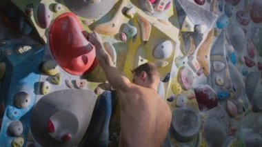 Atletik erkek kaya tırmanışçısı yapay bir kaya tırmanma duvarına tırmanır. Güçlü deneyimli bir atlet spor salonunda kaya tırmanışı yapar.