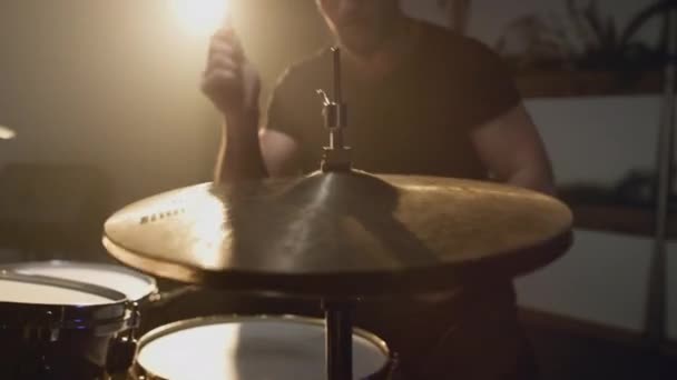Un joven y atractivo baterista masculino toca con un palo en un tambor. Hace golpes en los platillos de metal. Estudio de ensayo en casa para grabación de sonido y canciones. — Vídeos de Stock