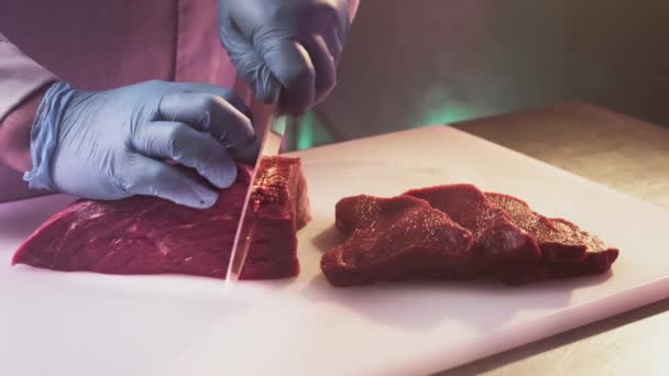 Ein Koch schneidet in einer Metzgerei mit einem Küchenmesser ein frisches rotes Roh-Filet. Scheiben Premium-Ribeye-Fleisch oder marmoriertes Rindfleisch. — Stockvideo