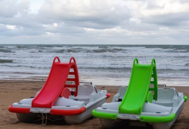  Fırtınalı bir sonbahar ya da kış öğleden sonrasında, kumsalda renkli slaytlı iki pedallı tekne. 