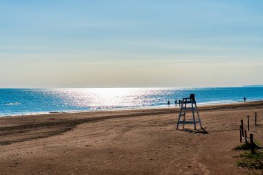 Neredeyse boş bir plaj, deniz üzerinde güneş ışığı, bir sonbahar ya da kış günü.