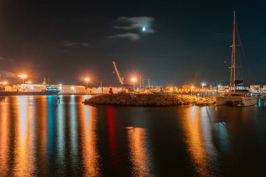 Gün batımında Gandia limanının deniz manzarasına uzun süre maruz kalmak, gemi ve depoların manzarası, ve bulutlu bir gökyüzü.