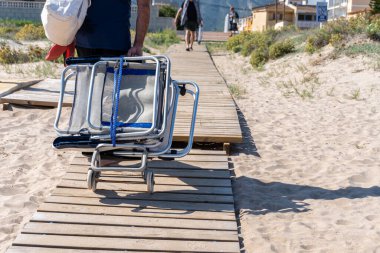 Tanımlanamayan bir adam plaj sandalyeli bir arabayı ahşap bir geçitte sürüklüyor..