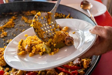 Bir restoranda beyaz tabakta Valencia 'dan (İspanya) tipik paella servis eden bir adam.