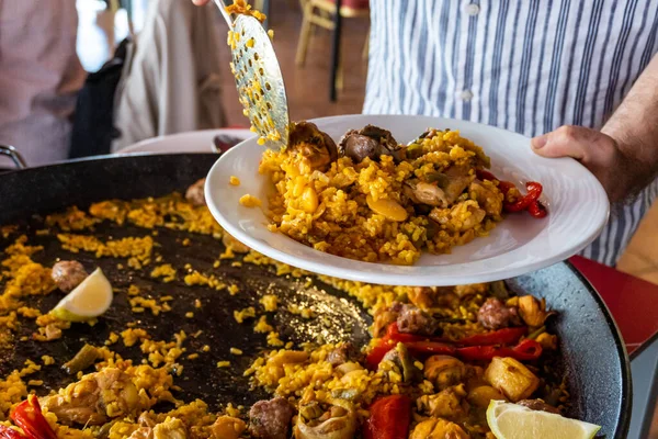 Bir restoranda beyaz tabakta Valencia 'dan (İspanya) tipik paella servis eden bir adam.